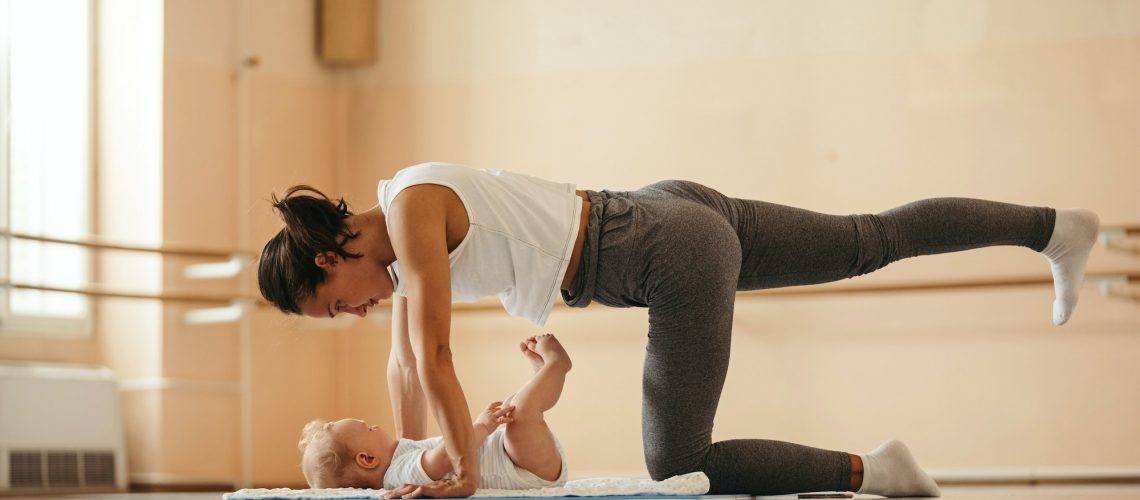 Athletic mother with baby doing stretching exercises in health club.
